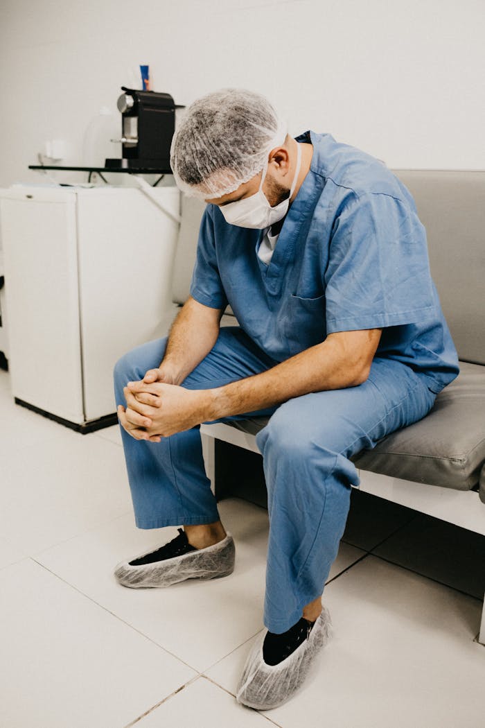 A male doctor in hospital attire sitting pensively, representing healthcare challenges.